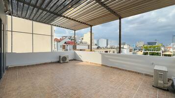 A rooftop terrace with a tiled floor, a pergola, and an air conditioning unit.