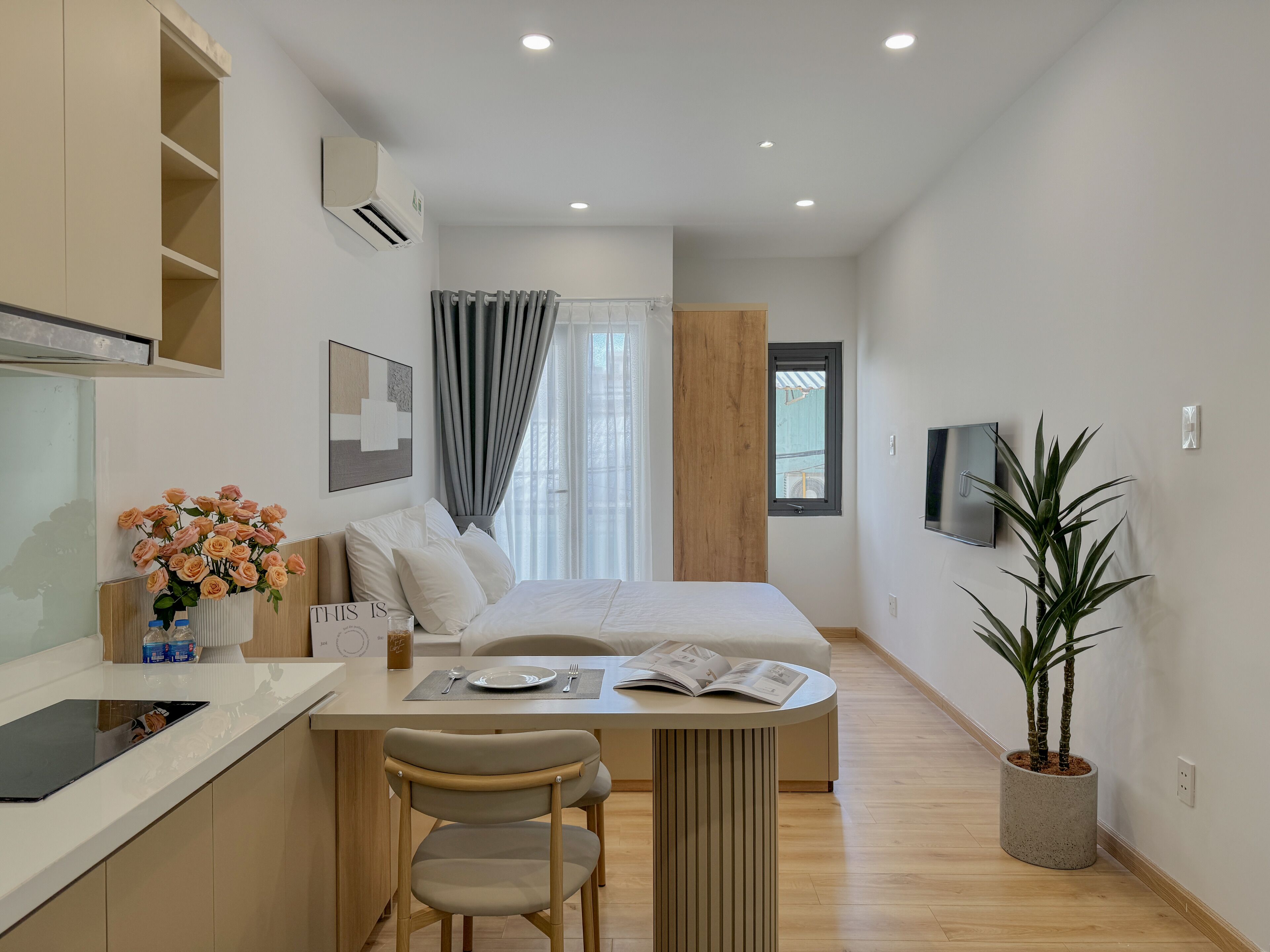 A modern hotel room with a bed, a desk, a chair, a potted plant, and a TV.