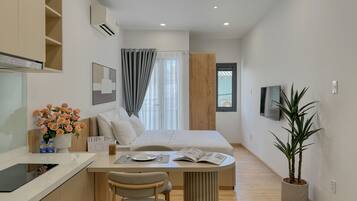 A modern hotel room with a bed, a desk, a chair, a potted plant, and a TV.