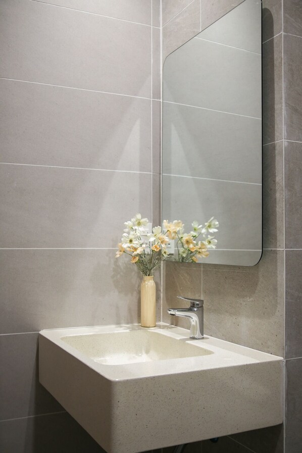 Baño con un espejo grande, un lavamanos y un jarrón con flores.