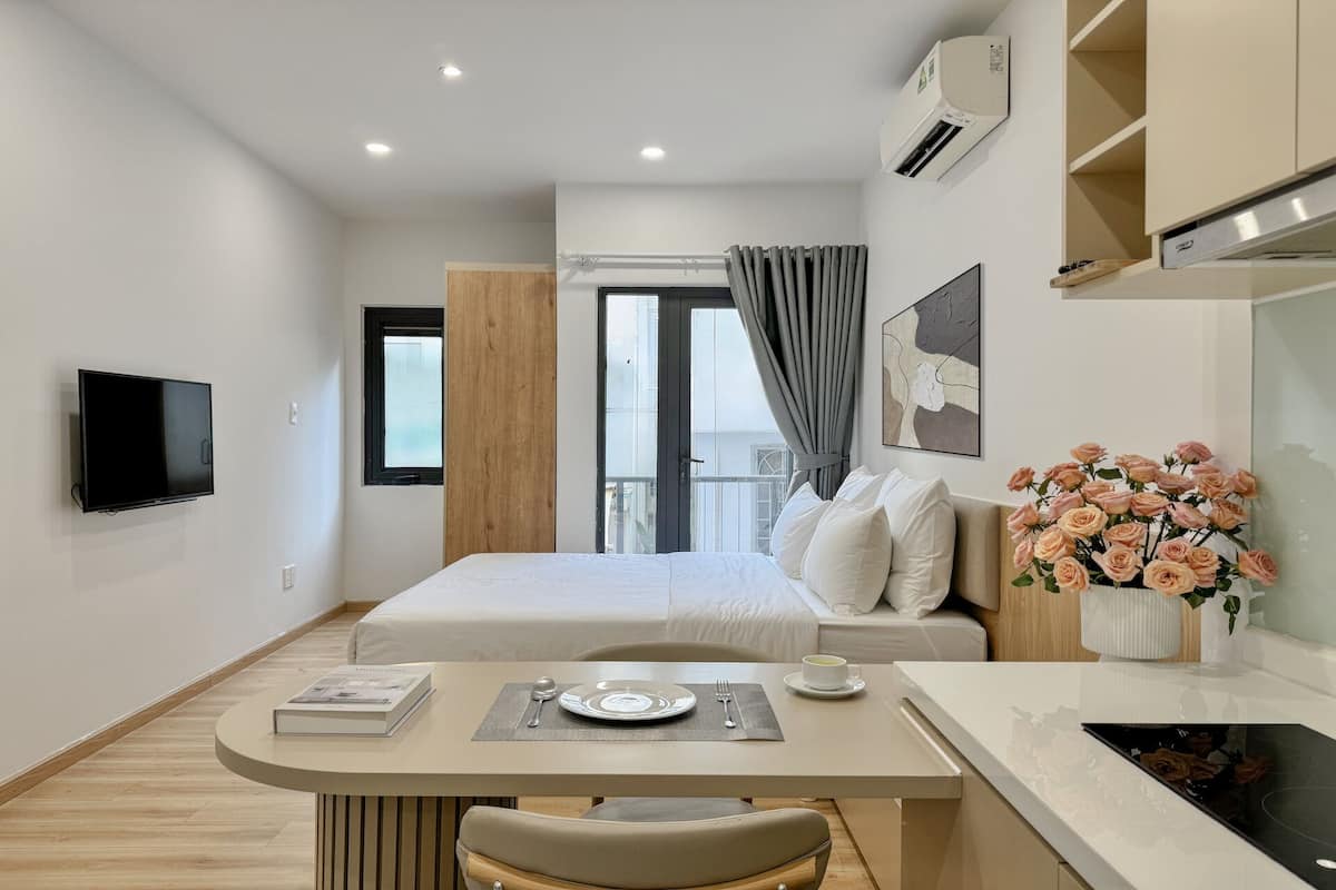 Une chambre d’hôtel moderne équipée d’un lit, d’une table à manger avec une chaise, d’un téléviseur fixé au mur et d’une fenêtre avec des rideaux.