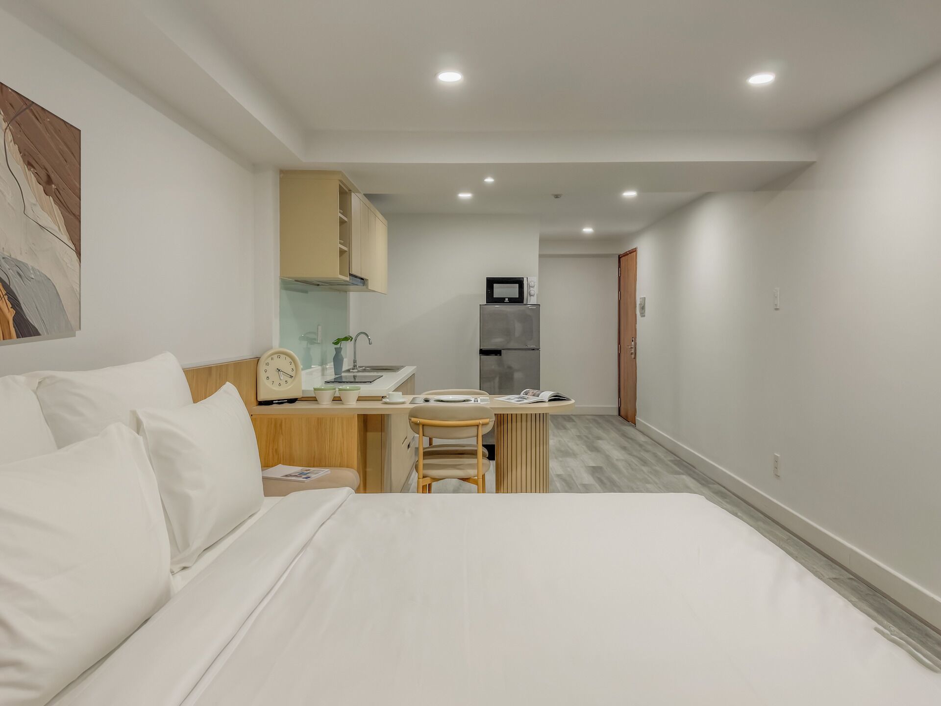 A modern hotel room with a large bed, a desk, a kitchenette, and a bathroom.
