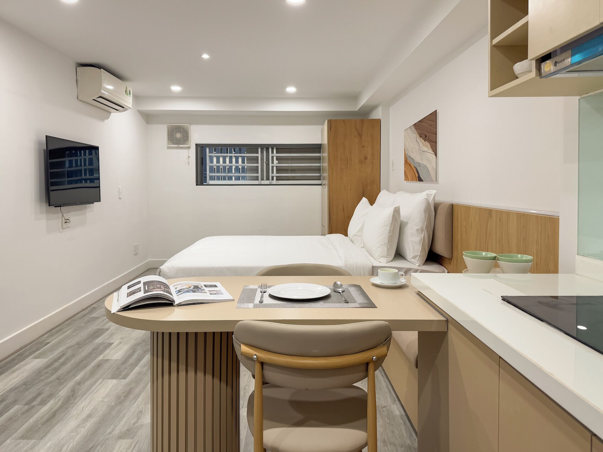 A modern hotel room with a bed, a desk with a chair, a television, and a window with blinds.