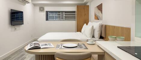 A modern hotel room with a bed, a desk with a chair, a television, and a window with blinds.