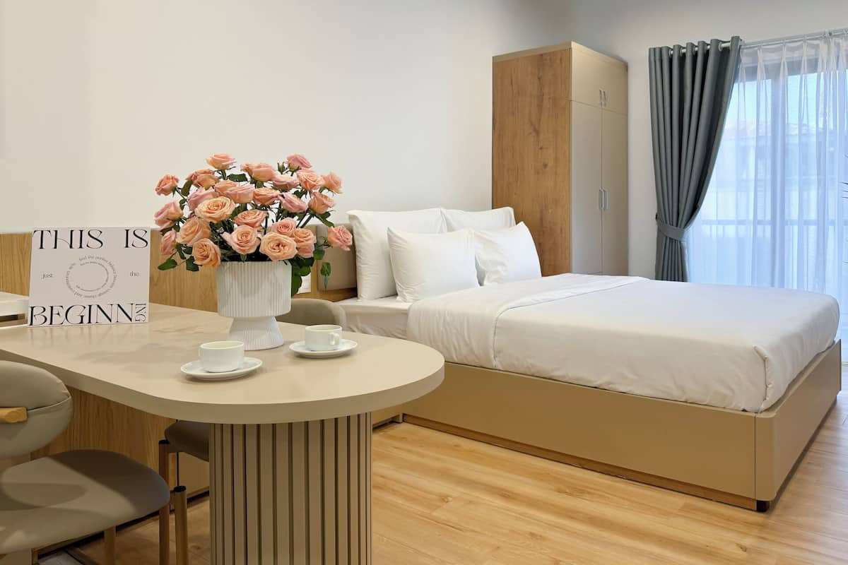 Une chambre d’hôtel moderne, avec un lit, une table de chevet ornée d’un vase de fleurs, un panneau indicateur et une vue sur l’extérieur à travers les rideaux.