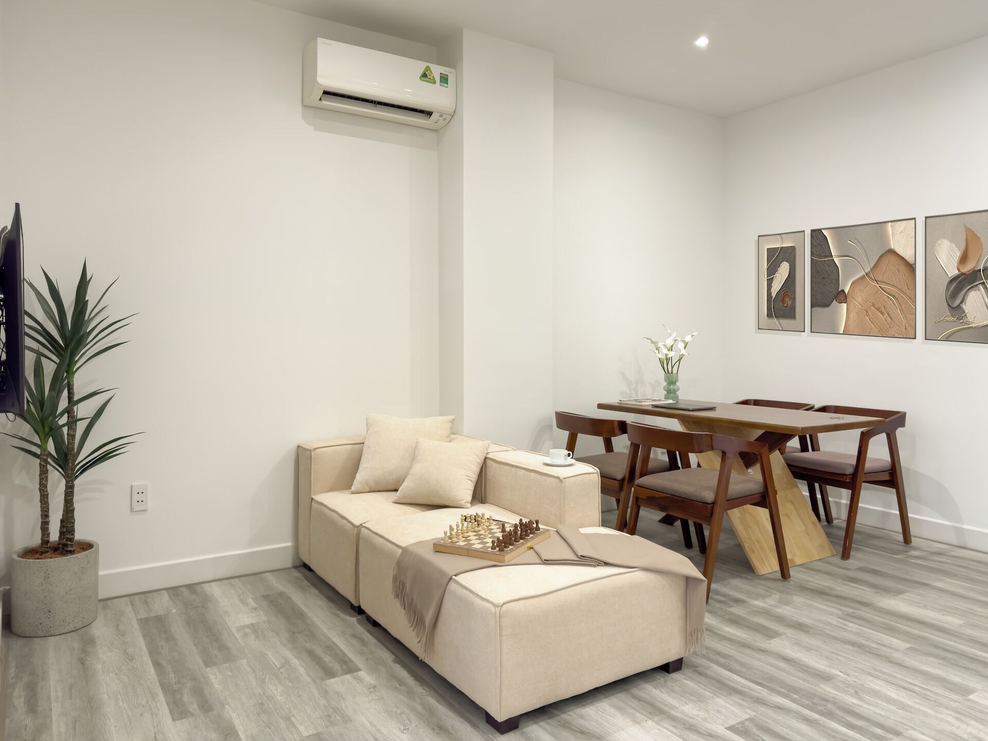 A modern living room with a beige sofa, a dining table, and a potted plant.