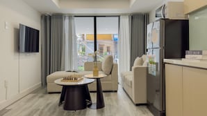 Una sala de estar moderna con un sofá, una mesa de centro, un televisor y una zona de cocina con refrigerador.