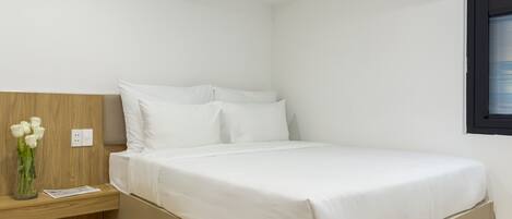 A minimalist bedroom with a bed, a nightstand, a vase with flowers, and a window with blinds.