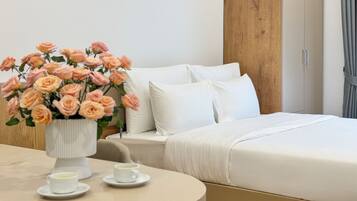 A neatly made bed with white linens, a vase of pink roses, and two cups of tea on a round table.