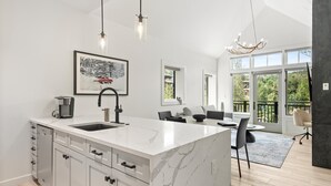 A modern kitchen with a marble island, a coffee machine, and a dining area with a view of the outdoors. - Skyline Loft | Capitol Peak Lodge #3323 | 1B/1B (Snowmass Village)