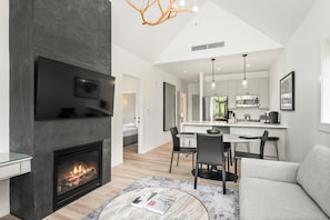 A modern living room with a fireplace, a dining area, and a kitchen in the background.