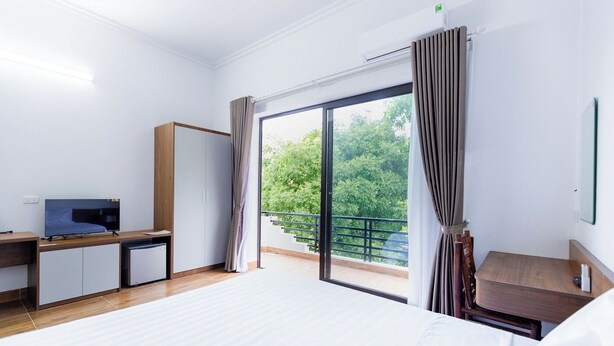 Une chambre d’hôtel comprenant un lit, un bureau avec un ordinateur, une télévision, une armoire et un balcon avec des rideaux.