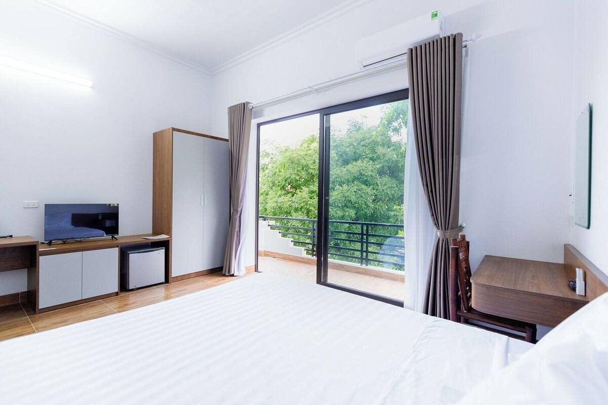 A hotel room with a bed, a desk with a computer, a TV, a wardrobe, and a balcony with curtains.