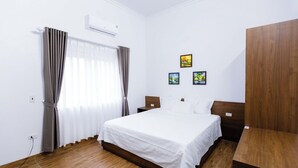 Une chambre d’hôtel comprenant un lit, deux tables de chevet, une commode en bois et un climatiseur fixé au mur.