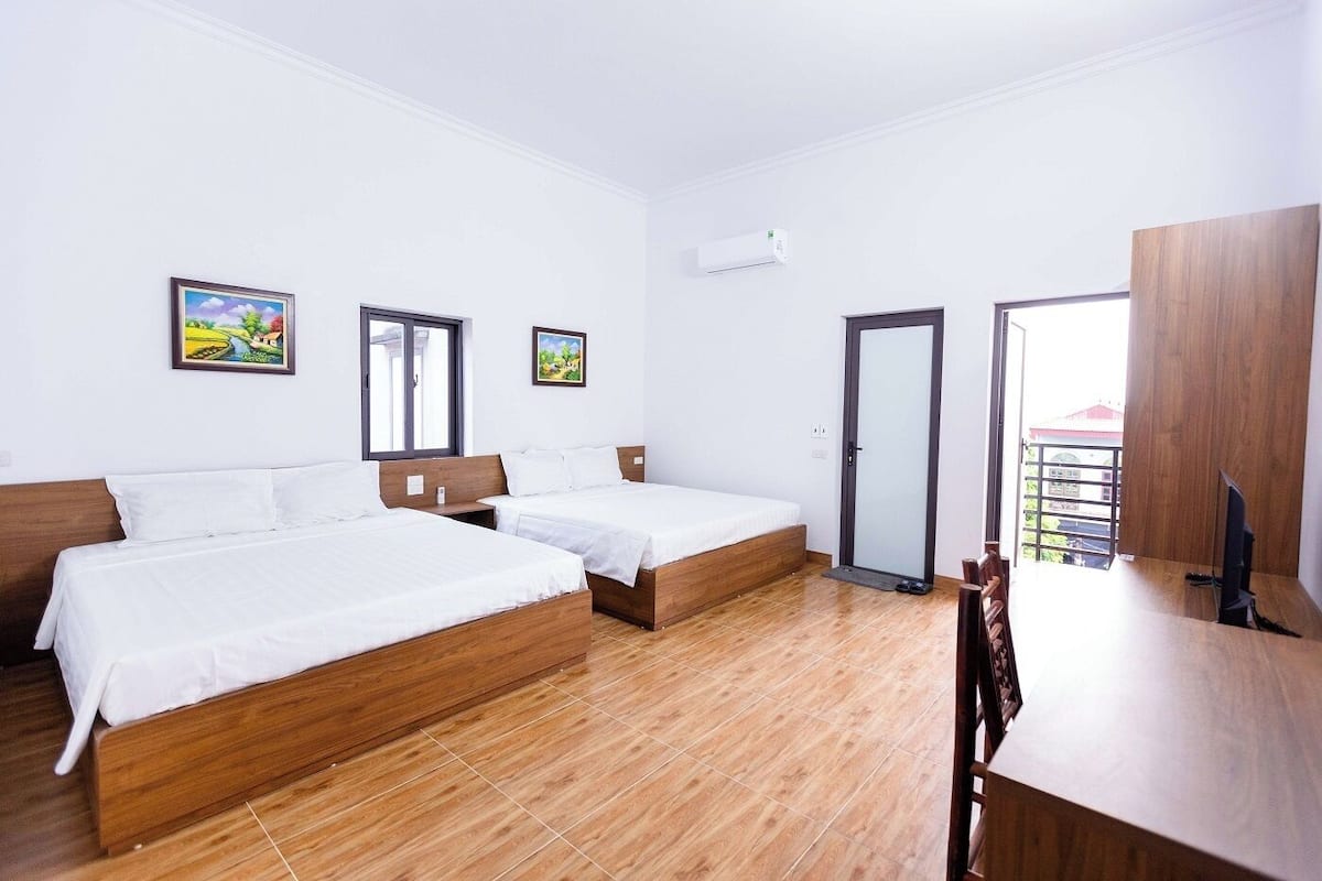 A hotel room with two beds, a wooden desk, a TV, and a balcony with a view.