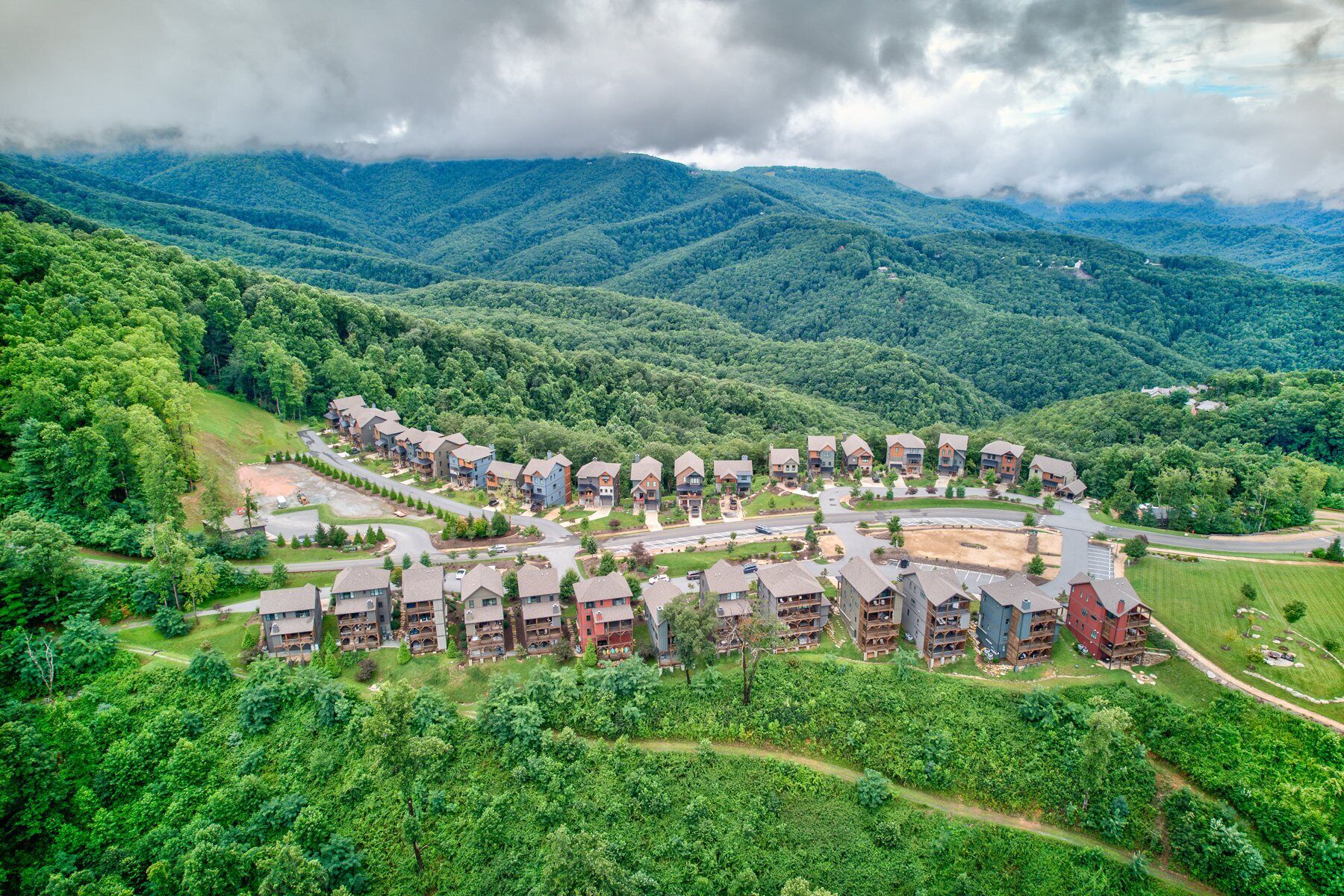 Un quartier résidentiel composé de plusieurs immeubles à deux étages, entouré d’une végétation luxuriante et avec des montagnes en toile de fond.