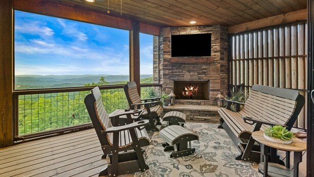 A wooden deck with a stone fireplace, outdoor seating, and a large window overlooking a mountainous landscape. - Western Ridge Lookout at Blue Ridge Mountain Club - community amenities with seasonal pool (Boone)