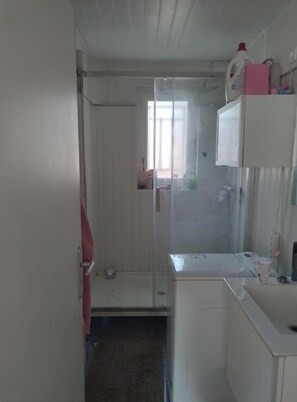 Un baño estrecho con paredes blancas, ducha, inodoro y zona de lavamanos.