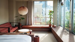 A modern hotel room with a large bed, a red sofa, a round coffee table, and a potted plant. - SOIL Nihonbashi Hotel (Tokyo)
