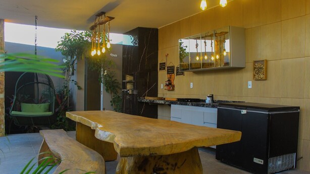A modern kitchen with a wooden table and bar, a hanging light fixture, and a large mirror above the counter. - Casa Bons ventos (Cruz)