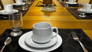 A conference room with a long table set for a meeting, equipped with chairs, plates, cups, and cutlery. - Casa Bons ventos (Cruz)