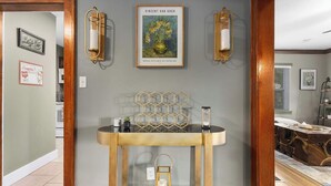 A room with a round wooden console table, a hexagonal metal wall art, and two wall-mounted light fixtures. - Sleeps 5 _ 2bedroom Home in Overland Park! (Overland Park)