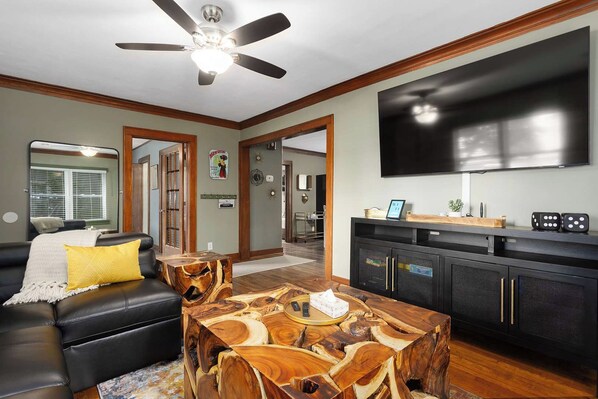 A modern living room with a black leather sofa, a wooden coffee table, a flat-screen TV, and a ceiling fan.