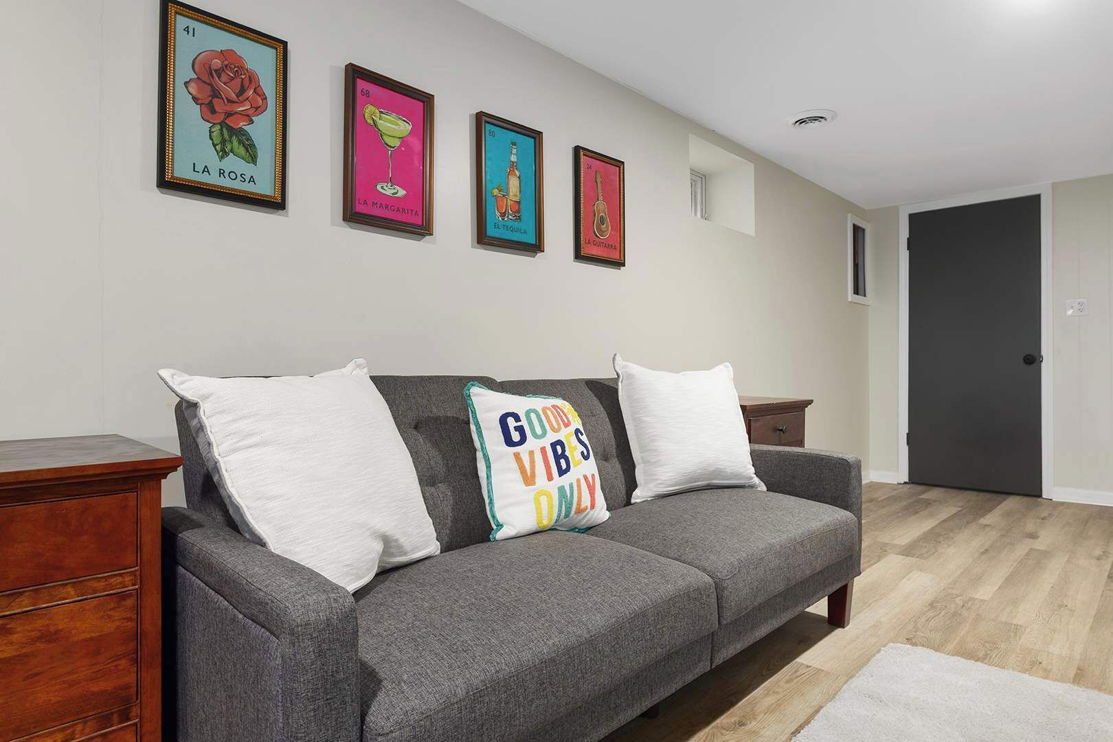 A grey sofa with white cushions in a room with wooden flooring, a wooden side table, and a door in the background.