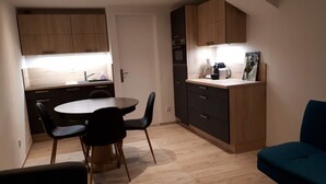 A compact kitchen with wooden cabinets, a round dining table with chairs, a coffee machine, and a framed picture on the counter. - 6-8 person apartment at the foot of the lifts, in a typical village (Champagny-en-Vanoise)