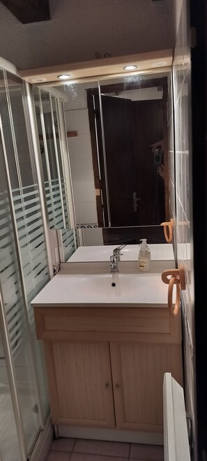 Une salle de bain avec un lavabo blanc, des meubles en bois, un miroir et un espace douche.