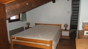 A bedroom with a wooden bed, a nightstand with a lamp, and a window with curtains. - 6-8 person apartment at the foot of the lifts, in a typical village (Champagny-en-Vanoise)