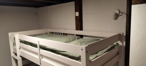 Een stapelbed met hoofdbord, een wandlamp en een deur aan de linkerkant.