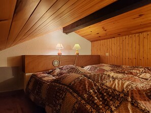 Een slaapkamer met een houten plafond, een bed met een geborduurd quilt en twee bedlampen.
