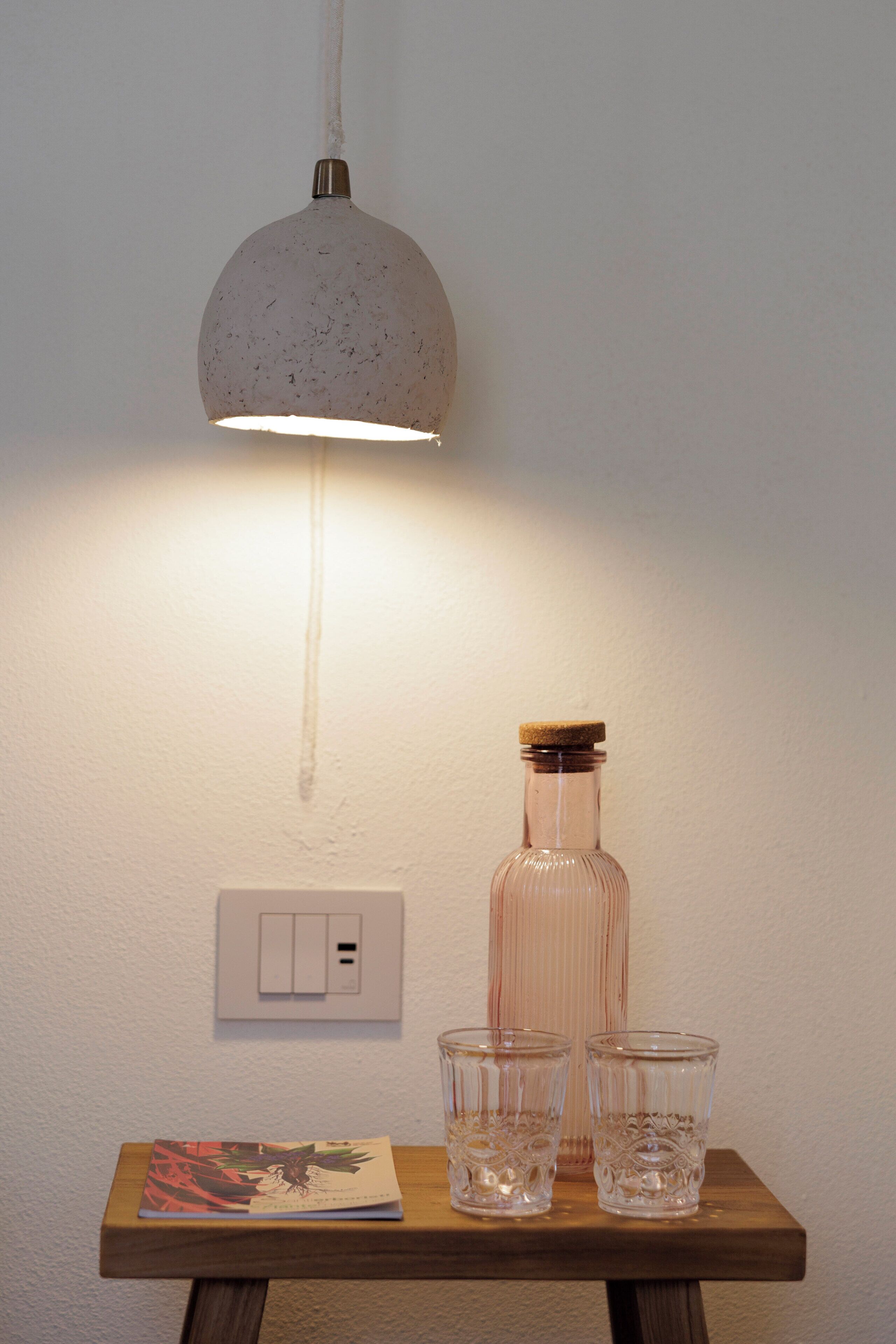 Ein Tisch mit einer Flasche, zwei Gläsern, einer Pendelleuchte und einem Lichtschalter.