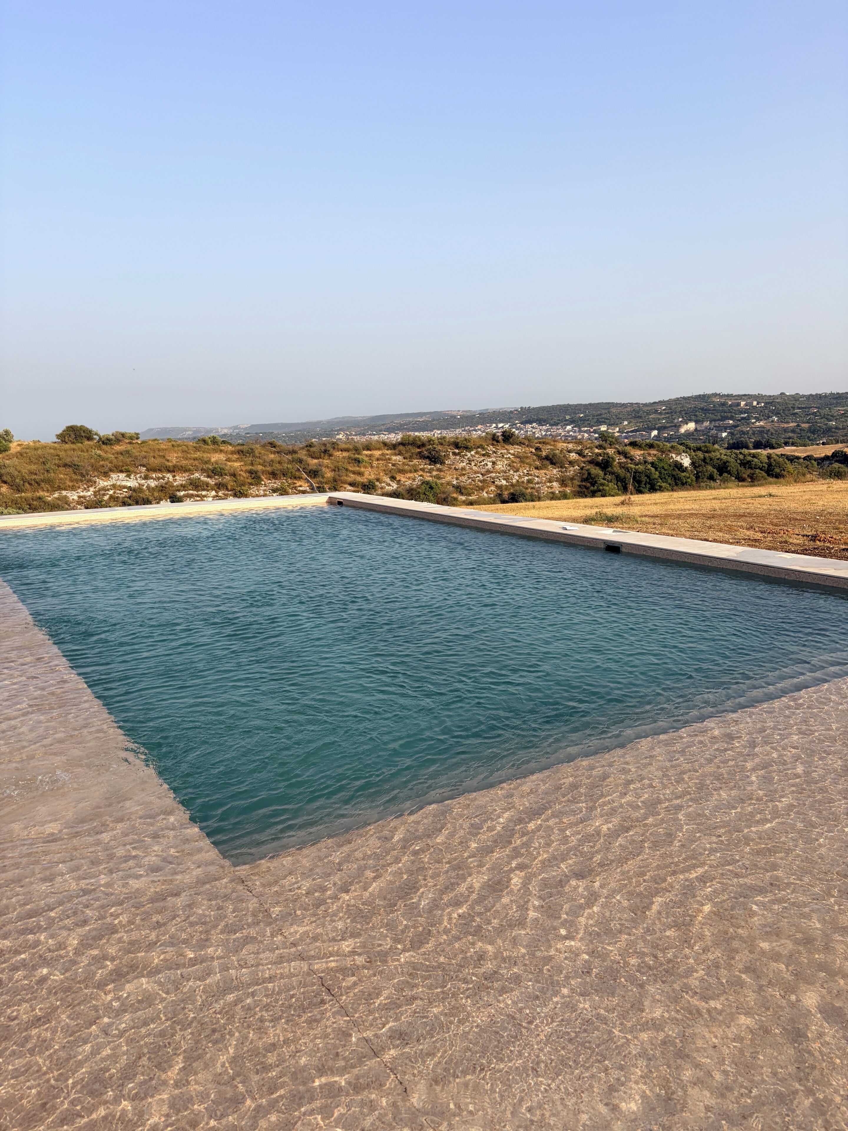 Ein rechteckiger Swimmingpool mit klarem, blauem Wasser, umgeben von einer Betonplattform.