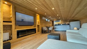 L’intérieur d’un chalet moderne, avec un grand téléviseur, des murs en bois, un coin repas et un espace salon confortable.