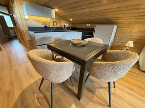 A cozy kitchen with wooden walls, a dining table with four chairs, and a small island with a bowl. - Apartment Nivalis - LES GETS: in the center and at the foot of the slopes (Les Gets)