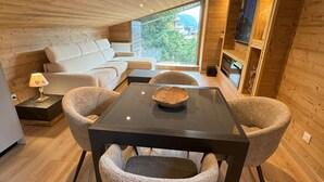 Un intérieur moderne avec un plafond en bois, une table centrale entourée de chaises, un canapé et une fenêtre donnant sur un paysage verdoyant.