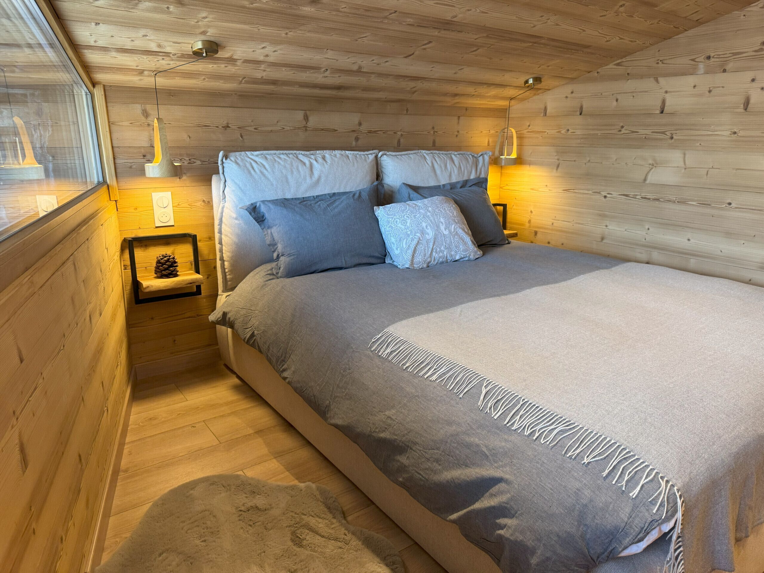 Une chambre confortable avec un plafond en bois, un lit avec une literie grise et deux lampes de chevet.