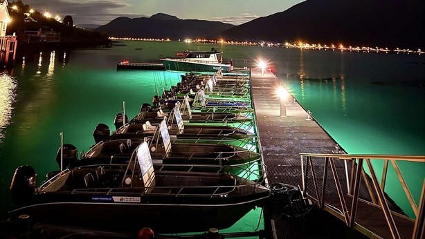Un muelle con barcos y un espigón que se adentra en aguas tranquilas, bajo un cielo nocturno con auroras boreales visibles.
