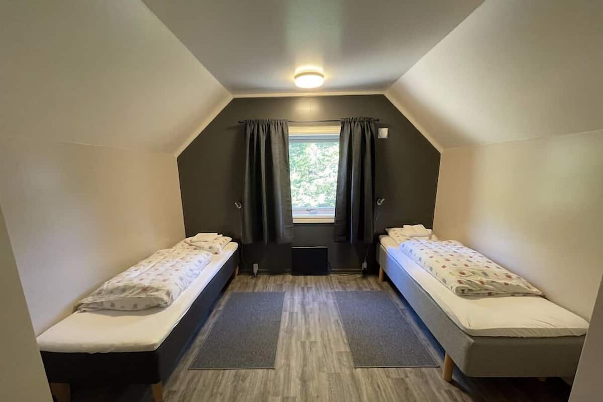 Una habitación pequeña y moderna con dos camas individuales, una ventana con cortinas e iluminación en el techo.
