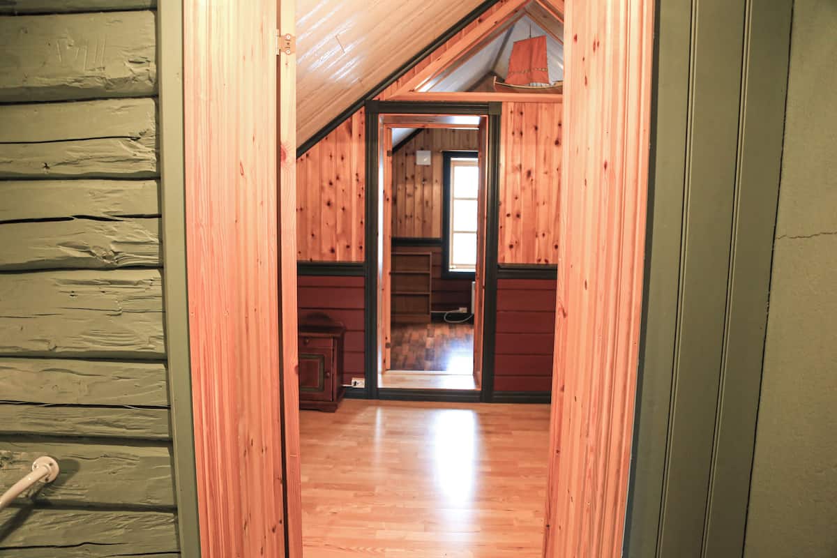 Un pasillo estrecho con paredes y suelo de madera, que conduce a una habitación con ventana y puerta.