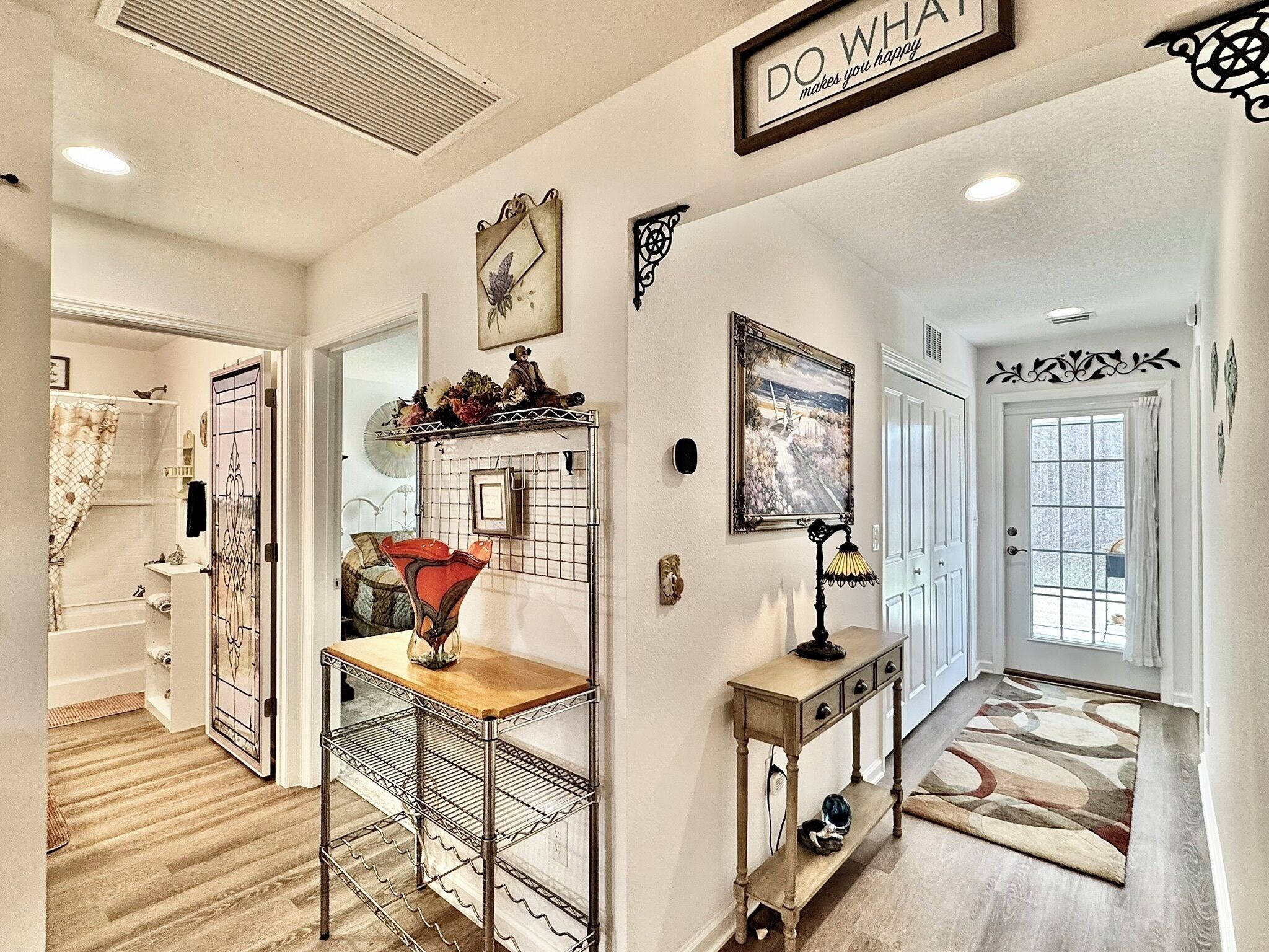 A well-lit hallway with a metal rack, a small table with a vase, a framed picture, and a decorative sign on the wall.