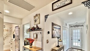 A well-lit hallway with a metal rack, a small table with a vase, a framed picture, and a decorative sign on the wall.