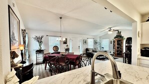 A modern kitchen with a marble countertop, stainless steel sink, and a dining area with a red tablecloth.