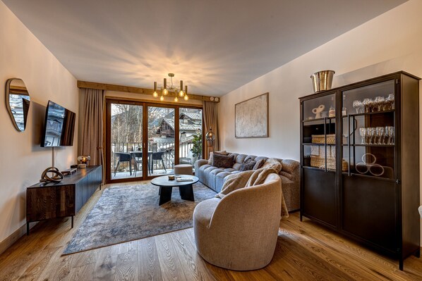 Un salon moderne comprenant un canapé, un fauteuil et une table basse, ainsi qu’un parquet et un meuble avec des portes en verre.