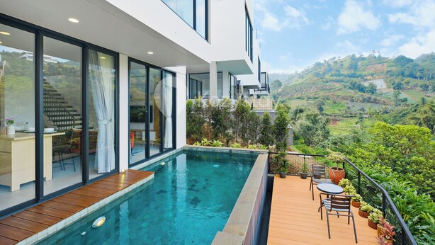 A modern house with a swimming pool, wooden deck, and a view of the countryside.