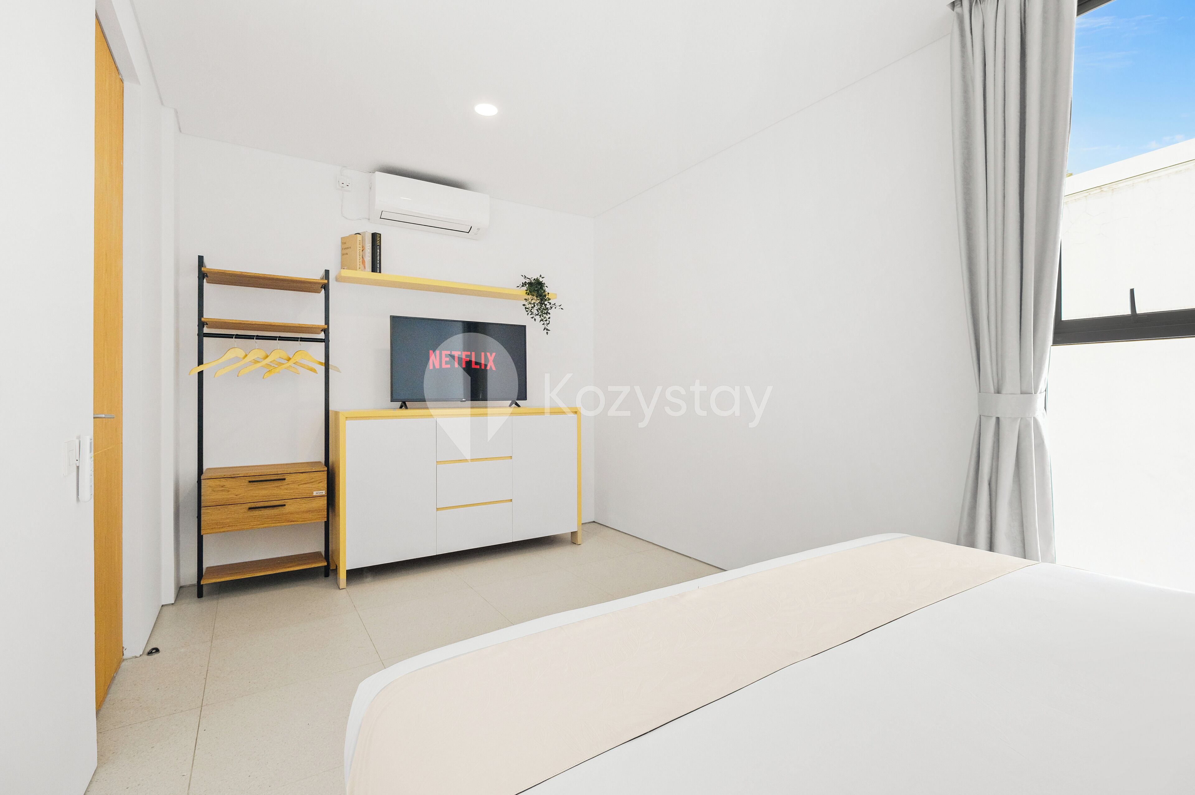 Un dormitorio moderno con cama, armario, televisor y estante con una planta.