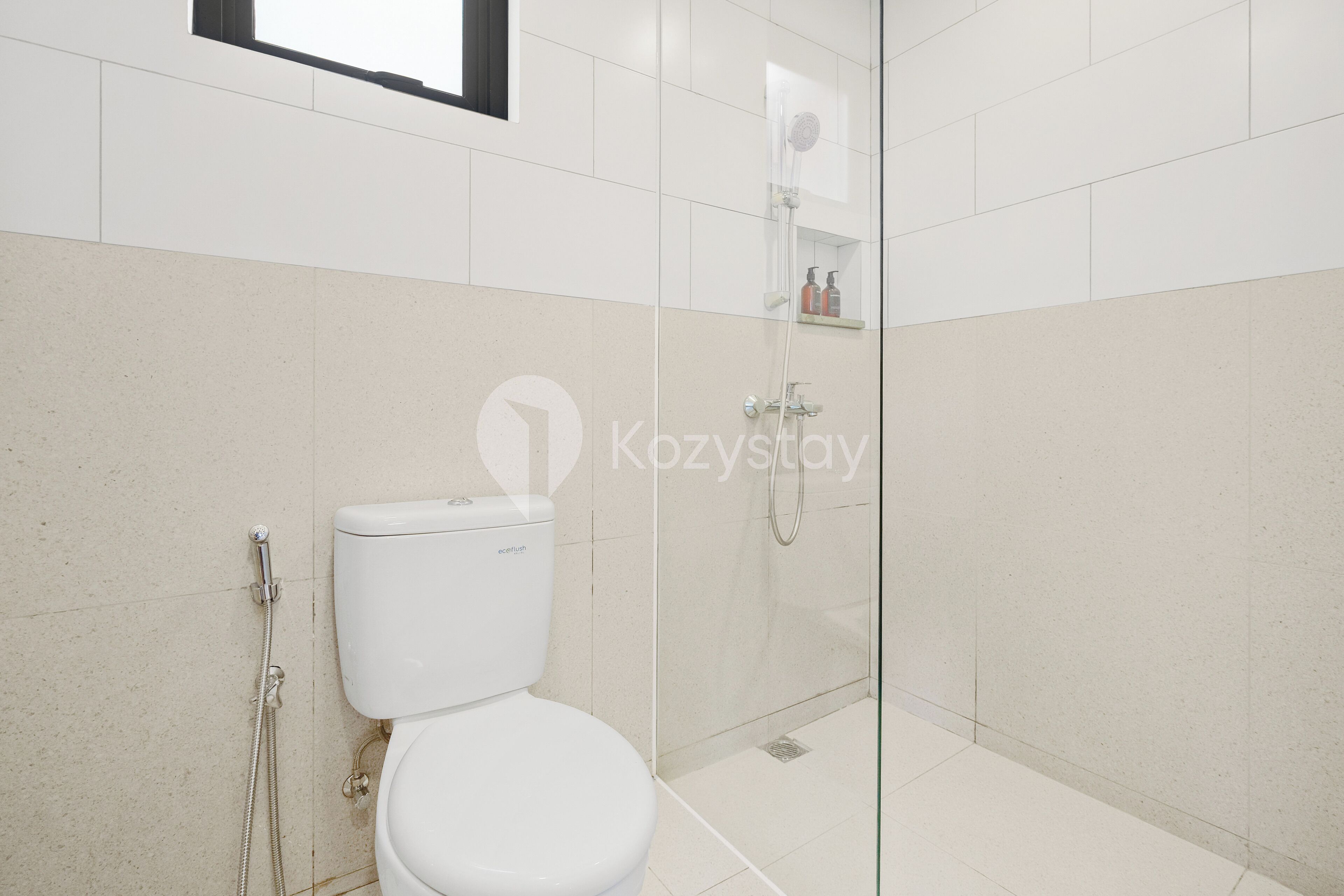 A modern bathroom with a toilet, a glass-enclosed shower, and a shelf with toiletries.