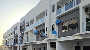 Un edificio residenziale a più piani con antenne paraboliche, balconi e auto parcheggiate.